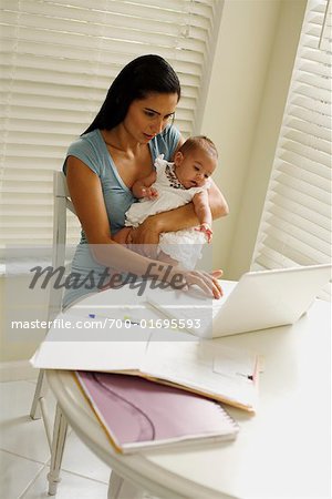 La mère travaille à l'ordinateur portable et tenant le bébé