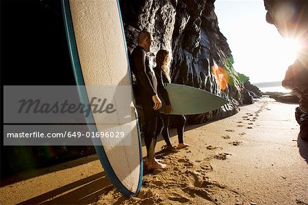 Couple Standing mit Surfbretter von großen Felsen.