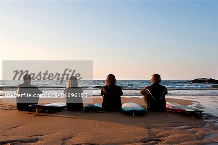 Four people sitting on the beach with surfboards.