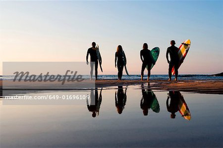 Four people standing on the beach with surfboards.