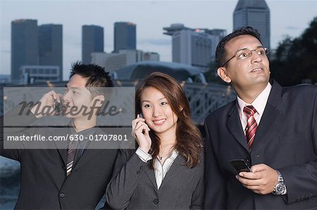 Deux hommes d'affaires et une femme d'affaires rassemblés et l'utilisation de téléphones mobiles, Singapour