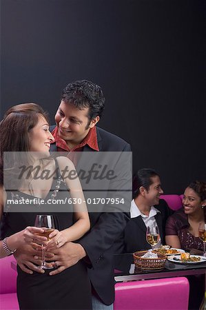 Young men embracing a young woman with a young couple sitting on a couch in the background