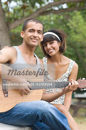 Portrait of a young man sitting with his girlfriend and playing a guitar