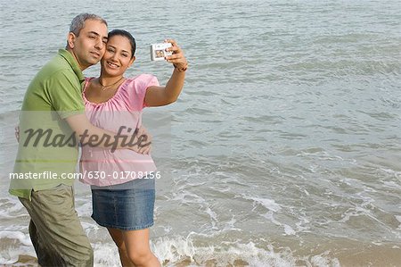 Mid adult couple taking a photograph of themselves on the beach