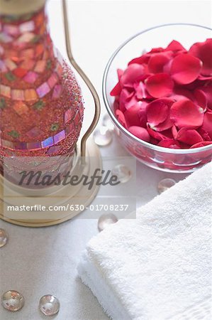 Close-up of rose petals in a bowl with a stack of towels and a lantern