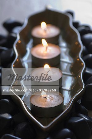 Gros plan de quatre bougies d'aromathérapie brûlant dans un plateau de galets noirs