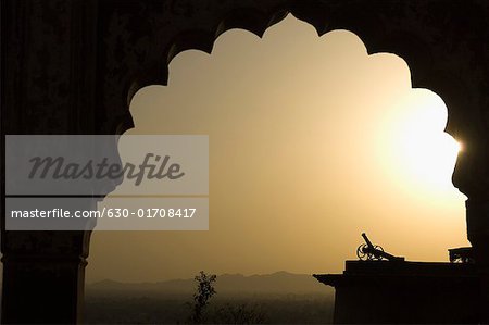 Silhouette der eine Kanone, die durch einen Bogen bei Sonnenuntergang betrachtet, Neemrana Fort, Neemrana, Alwar, Rajasthan, Indien