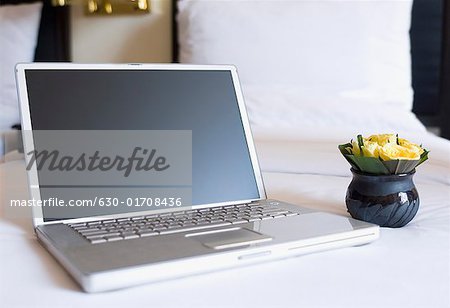 Close-up of a laptop and a flower vase on the bed in a hotel room