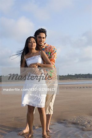 Porträt eines jungen Mannes, der eine junge Frau von hinten umarmen, am Strand