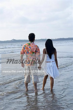 Vue arrière d'un standing de jeune couple avec main dans la main sur la plage