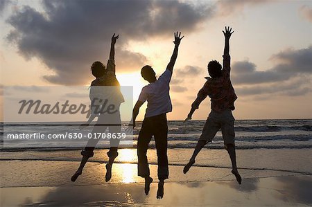 Rear view of three young men jumping with their hands raised on the beach