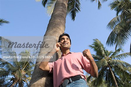 Vue d'angle faible d'un jeune homme appuyé contre un arbre et parler sur un téléphone mobile