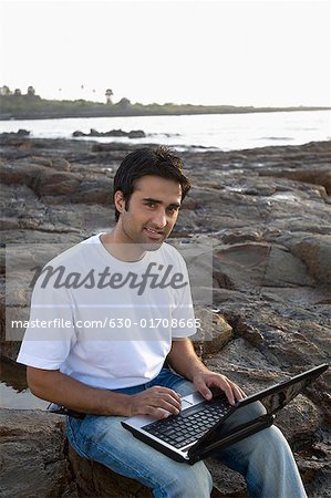 Porträt eines jungen Mannes einen Laptop auf dem Schoß halten und Lächeln, Madh Island, Mumbai, Maharashtra, Indien