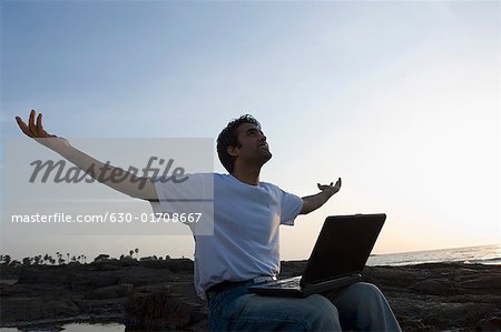 Profil de côté d'un jeune homme assis sur une côte avec ses bras tendus, île Madh, Mumbai, Maharashtra, Inde
