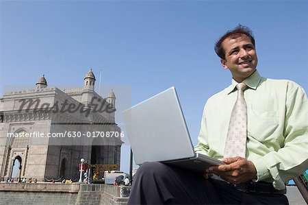 Unternehmer, die holding Laptop vor Denkmal, Gateway of India, Mumbia, Maharashtra, Indien,
