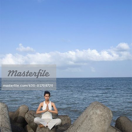 Young woman doing yoga on a rock