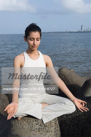 Jeune femme faisant du yoga sur une roche