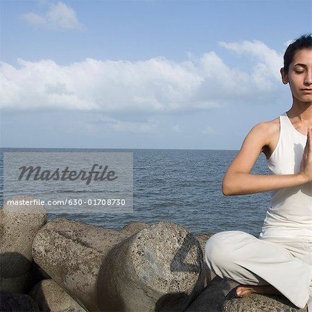 Young woman doing yoga on a rock