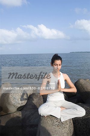 Jeune femme faisant du yoga sur une roche