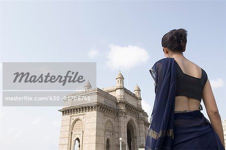 Rückansicht einer jungen Frau stehend mit einem Denkmal im Hintergrund, Gateway Of India, Mumbai, Maharashtra, Indien