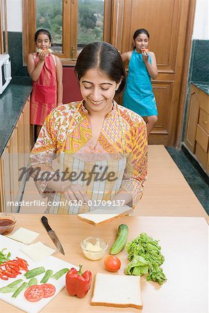 Frau mittleren Alters, Verbreitung von Butter auf ein Stück Brot mit ihren Töchtern im Hintergrund
