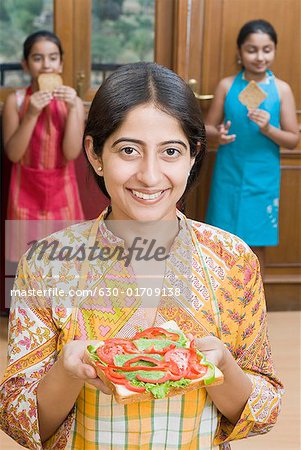 Close-up of a mid adult woman holding a sandwich with her daughters in the background