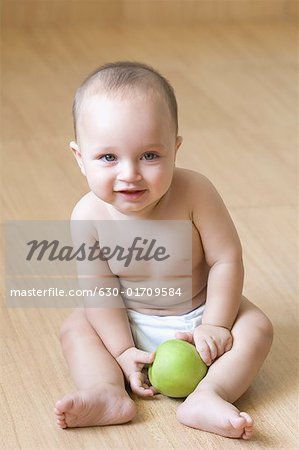 High angle view of a baby boy sitting on the hardwood floor and holding an apple