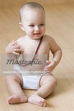 Baby boy sitting on the hardwood floor and wearing a mala