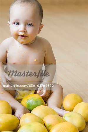 Portrait of a baby sitting on the hardwood floor and getting messy with mangoes