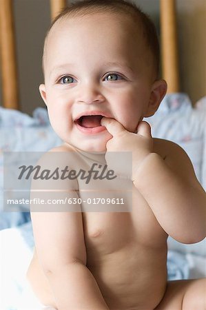 Close-up of a baby boy sitting in a crib and putting his finger in his mouth