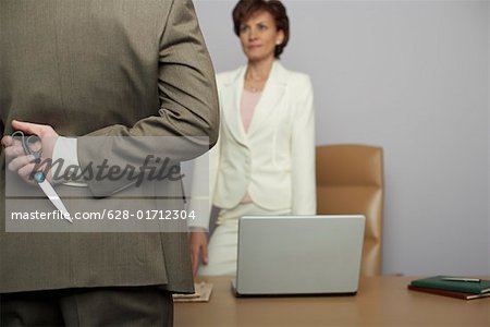 Businessman holding scissors behind back, facing businesswoman in office
