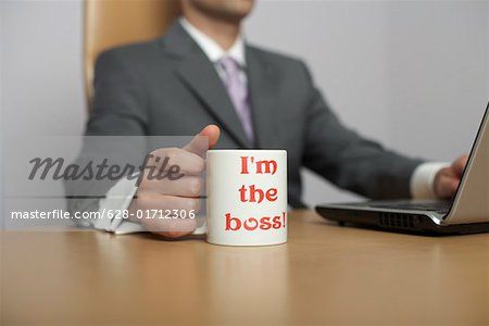 Homme d'affaires utilisant un ordinateur portable, je suis le patron ! Tasse à café en premier plan
