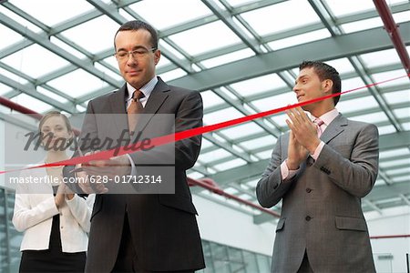 Businessman cutting red ribbon, colleagues clapping