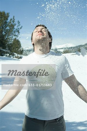 Young man standing in snowy landscape with arms out, head back and eyes closed, under falling snow