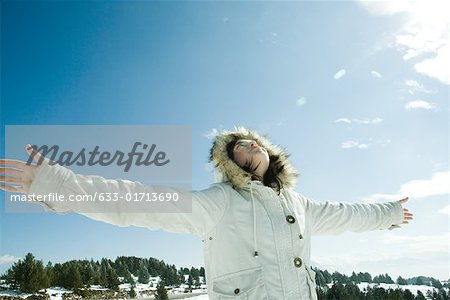 Teen girl standing in snowy landscape with arms out, head back, low angle view