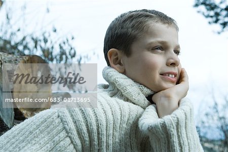 Boy wearing wool sweater, hand under chin, looking away