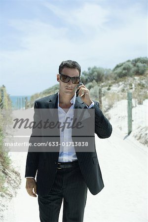 Businessman walking on path through dunes, using cell phone
