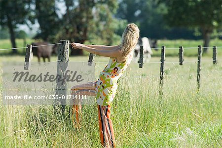 Jeune femme tenant à la clôture rural, vue latérale