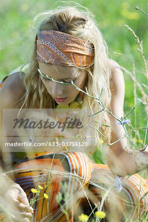 Jeune femme accroupie pour cueillir des fleurs dans le champ, gros plan