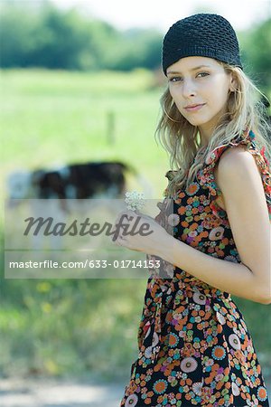 Fleur holding jeune femme en milieu rural, souriant à la caméra