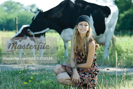 Young woman crouching in front of cows, smiling at camera