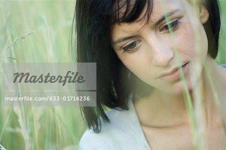 Young woman in tall grass, looking down, portrait