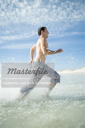 Young man running through surf on beach, full length, side view