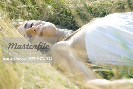 Young woman reclining in tall grass, smiling at camera