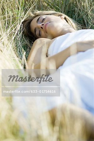 Young woman reclining in tall grass with eyes closed