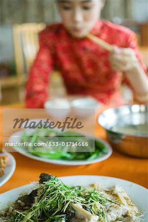 Young woman wearing traditional Chinese clothing, eating with chopsticks, focus on food in foreground