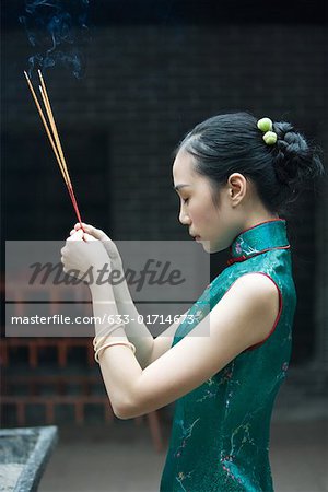 Jeune femme portant des vêtements traditionnels chinois, brandissant des encens, vue latérale