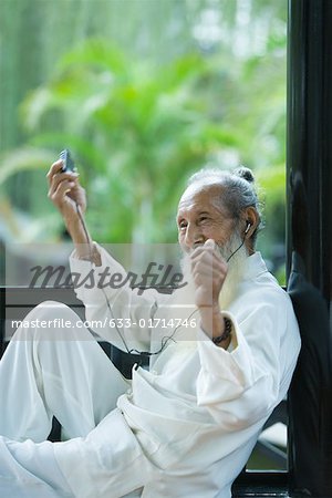 Elderly man wearing traditional Chinese clothing, listening to MP3 player, moving arms and smiling