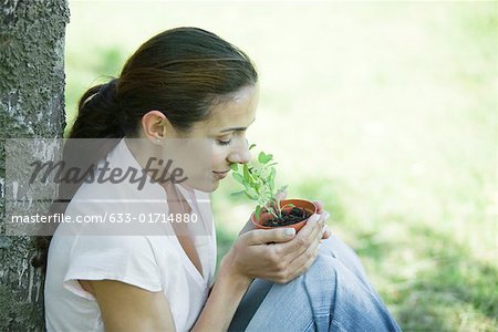 Woman sitting outdoors, smelling pot of herbs