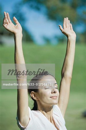 Woman outdoors in sun with arms raised, smiling, eyes closed